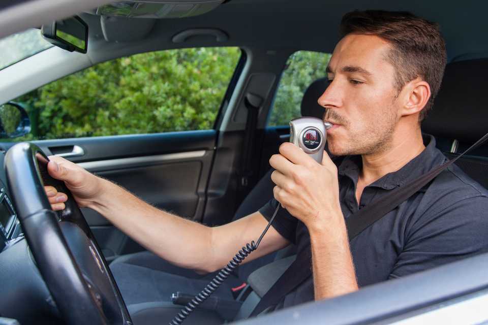man blows into breathalyzer for drunk driving check